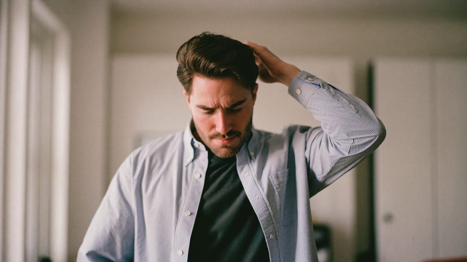 Man in his late 20s running a hand through his hair at the temple, checking for thinning