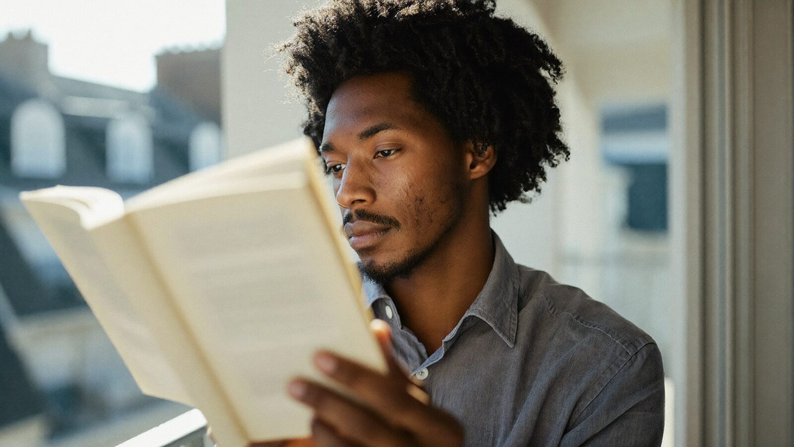 Man in his late 30s reading a book on a bright balcony