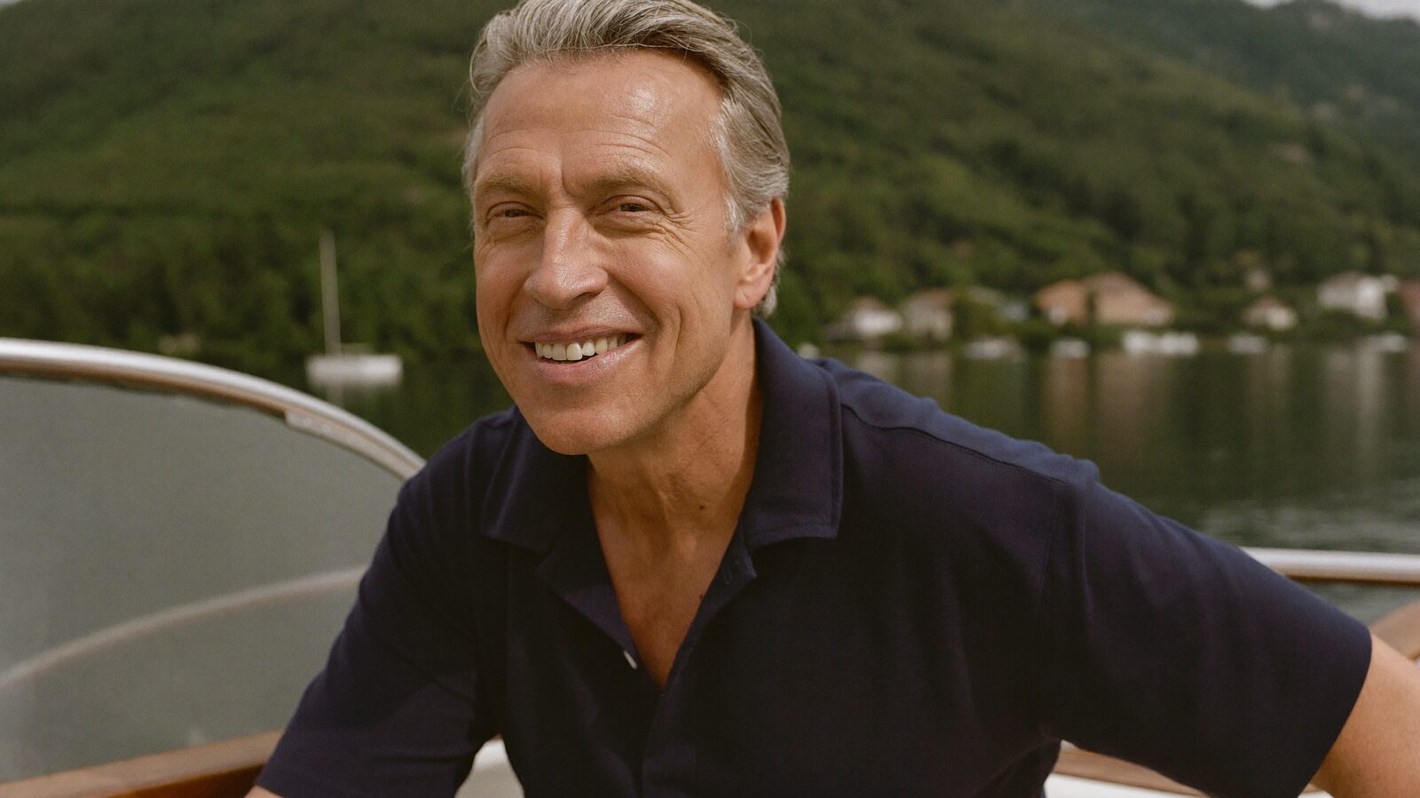 Smiling man in his 50s with full salt-and-pepper hair on a boat deck with a lake behind