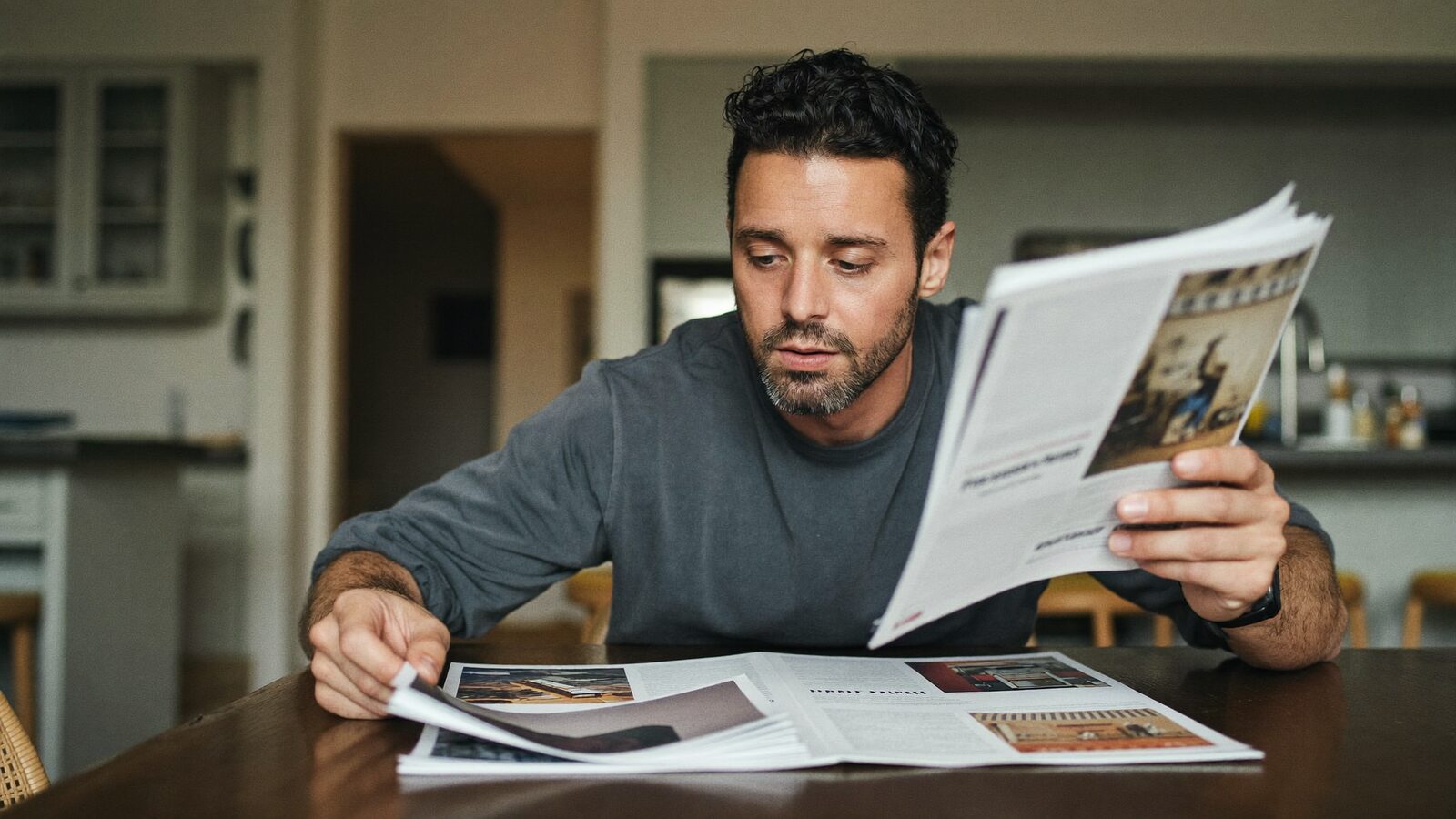 Man in his 30s reading clinic brochures at a kitchen table while comparing options
