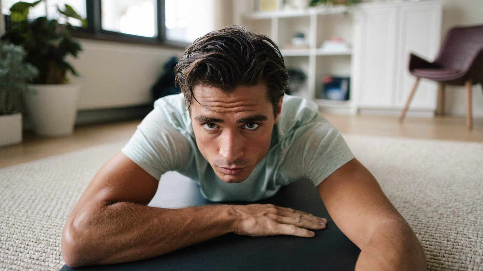 Man in his 30s with thick dark hair resting on a yoga mat during a light home workout